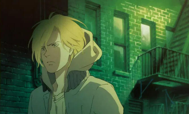 A promotional image of Ash Lynx walking towards the left side of the composition. He has a serious expression and wears a hooded jacket. Behind him is a brick building with a fire escape. There is a green tint to the image.